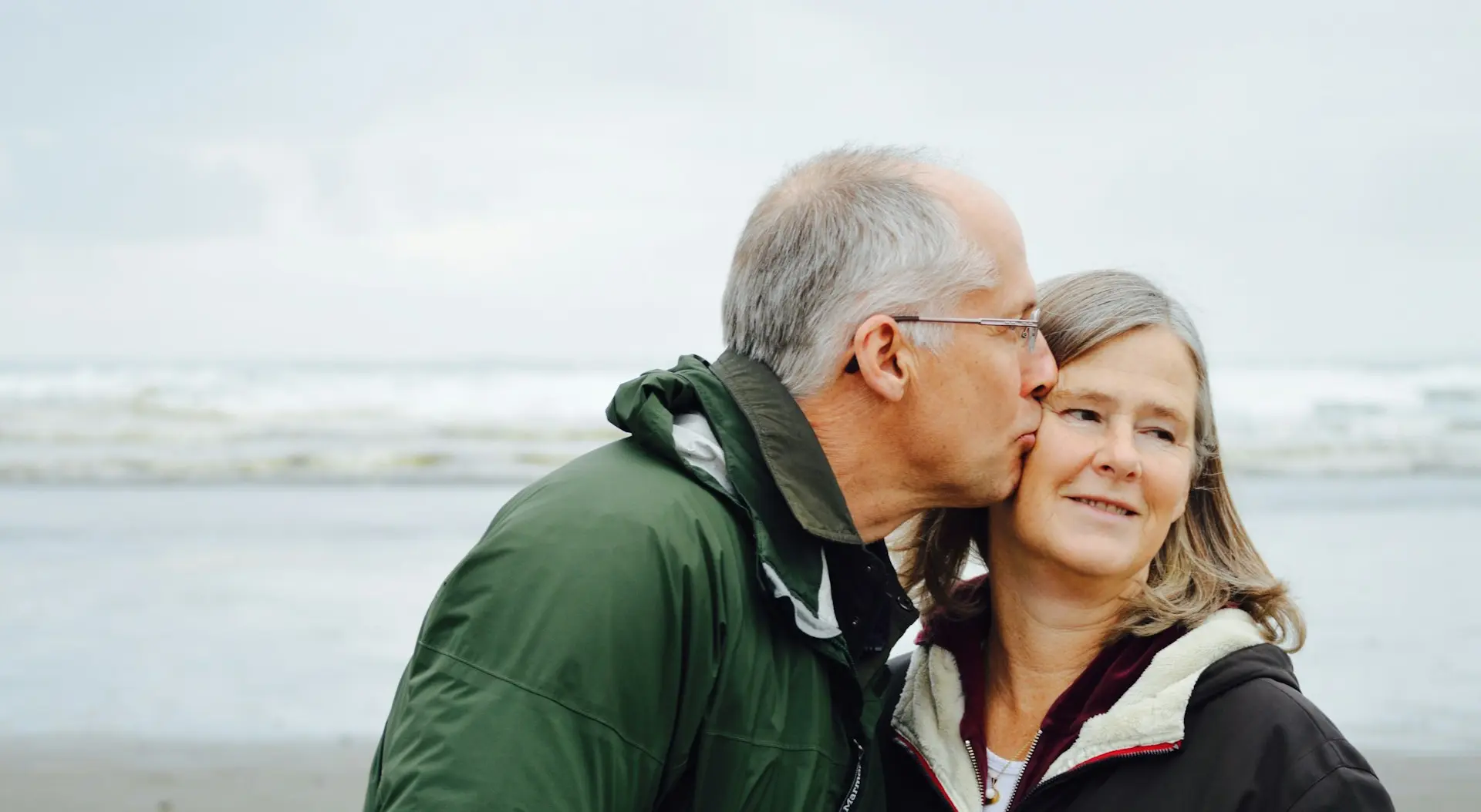 man kissing woman on check beside body of water